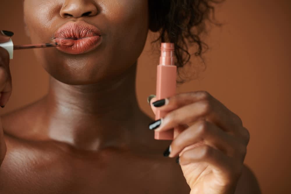 Imagem de mulher aplicando batom líquido marrom nos lábios