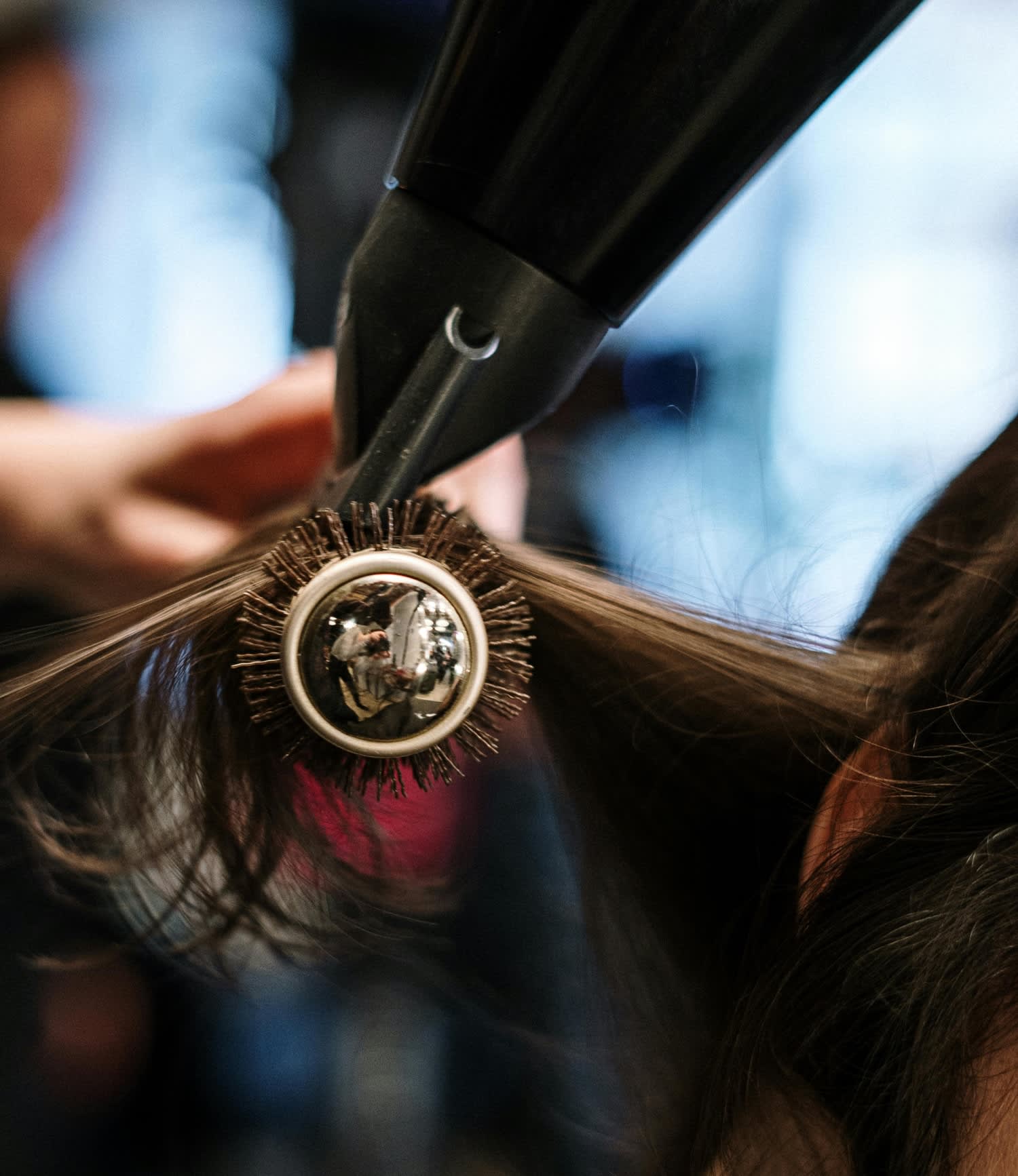 Secador de cabelo com uma escova secando uma mecha de cabelo comprido