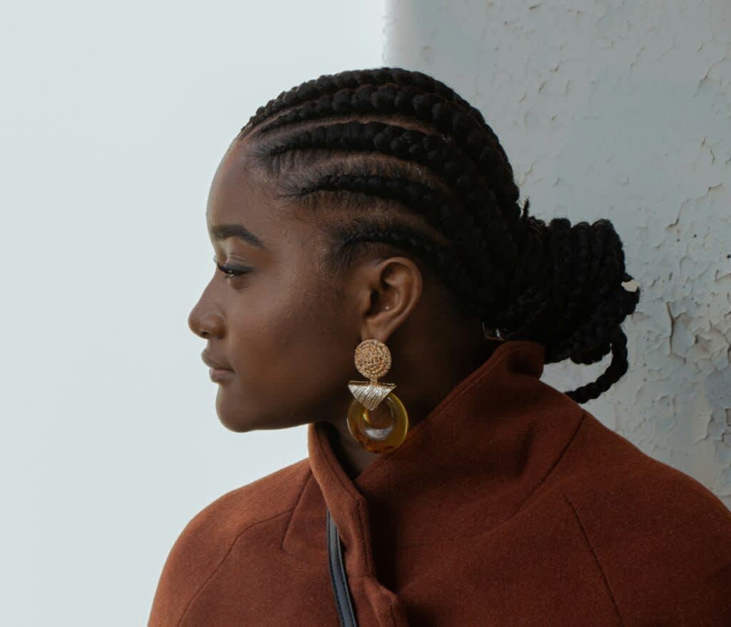 Mulher de perfil com tranças presas num coque e brincos grandes.