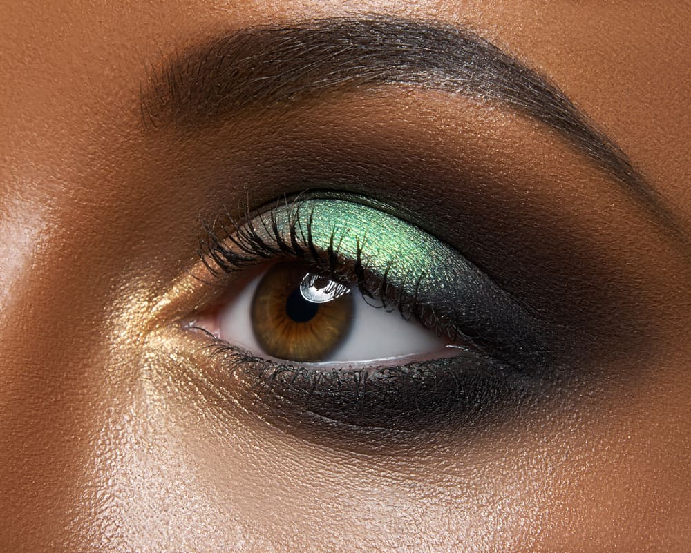 Imagem foca em olhos maquiados com sombra verde e cílios longos e destacados
