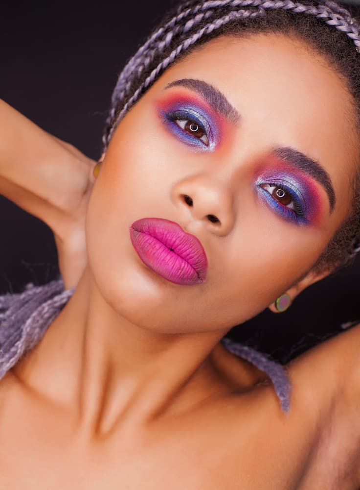 Mulher usando maquiagem com sombra degradê colorida e batom rosa