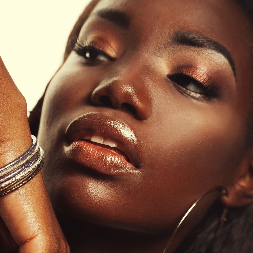 Mulher usando maquiagem em tons metálicos e com efeito glow