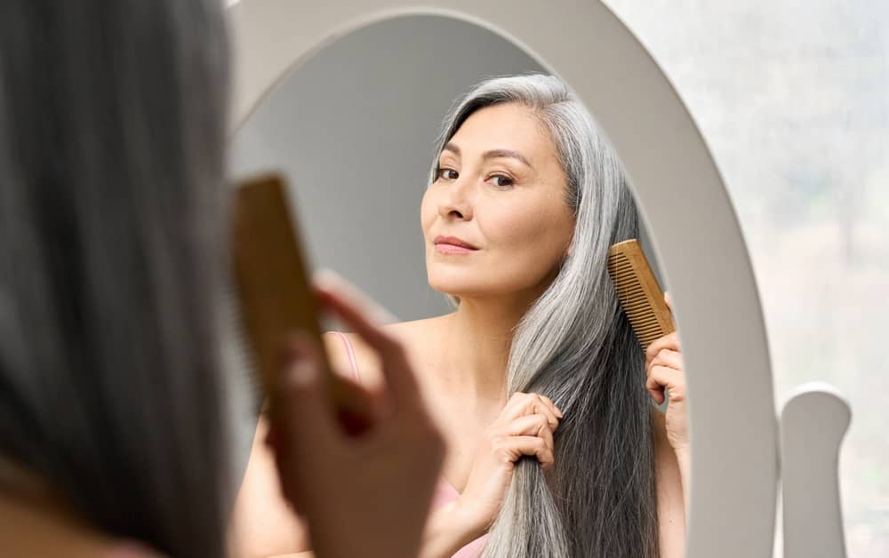 Imagem de mulher em frente ao espelho penteando o cabelo