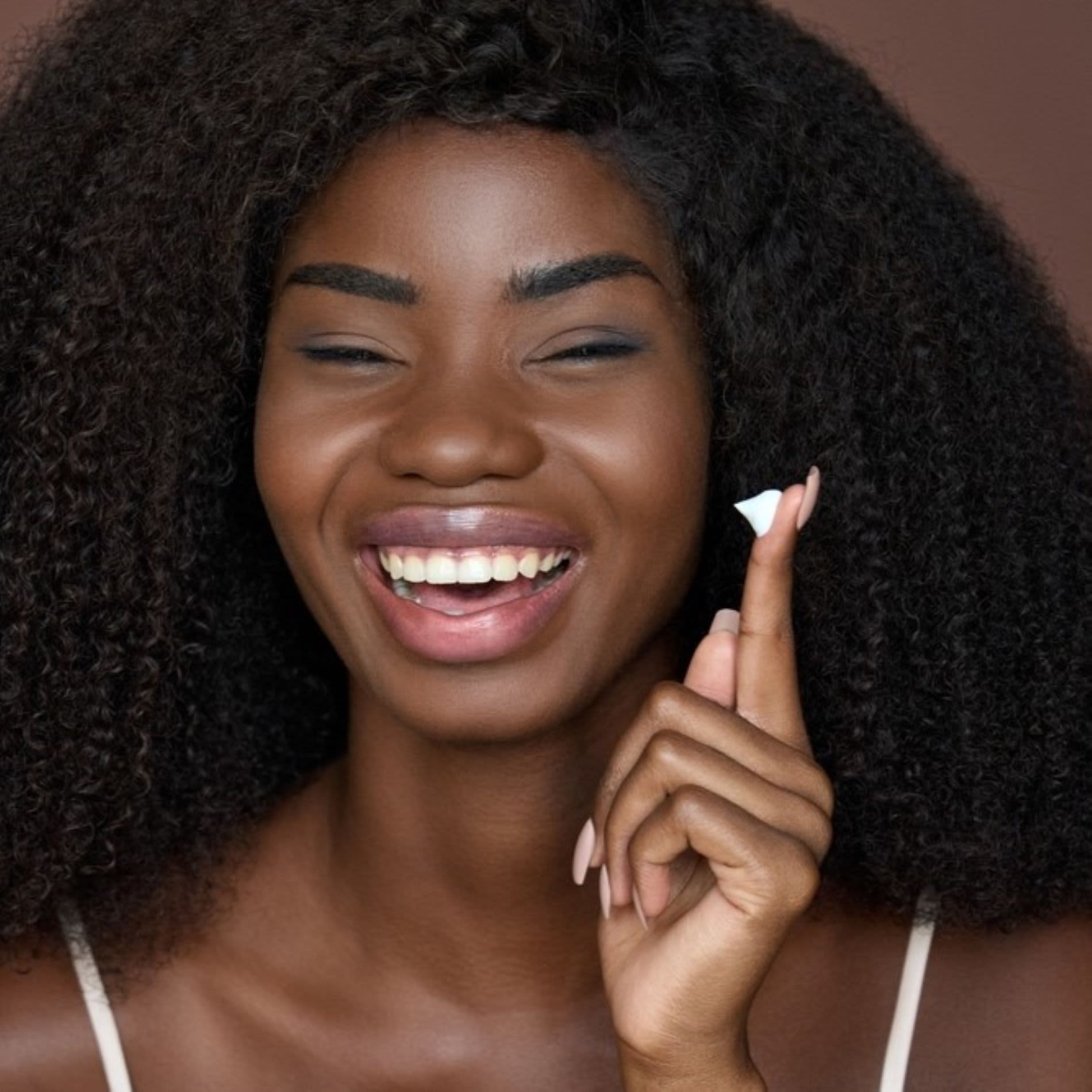 Mulher sorrindo ao aplicar protetor solar na pele
