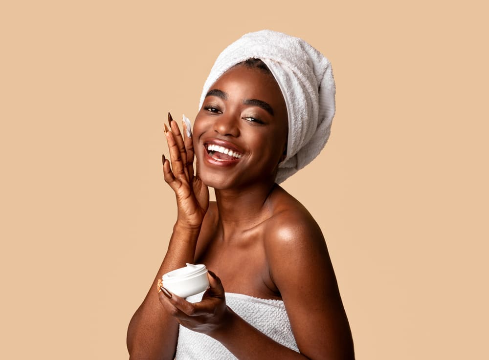 Imagem de mulher sorrindo enquanto aplica um produtos de skincare na pele
