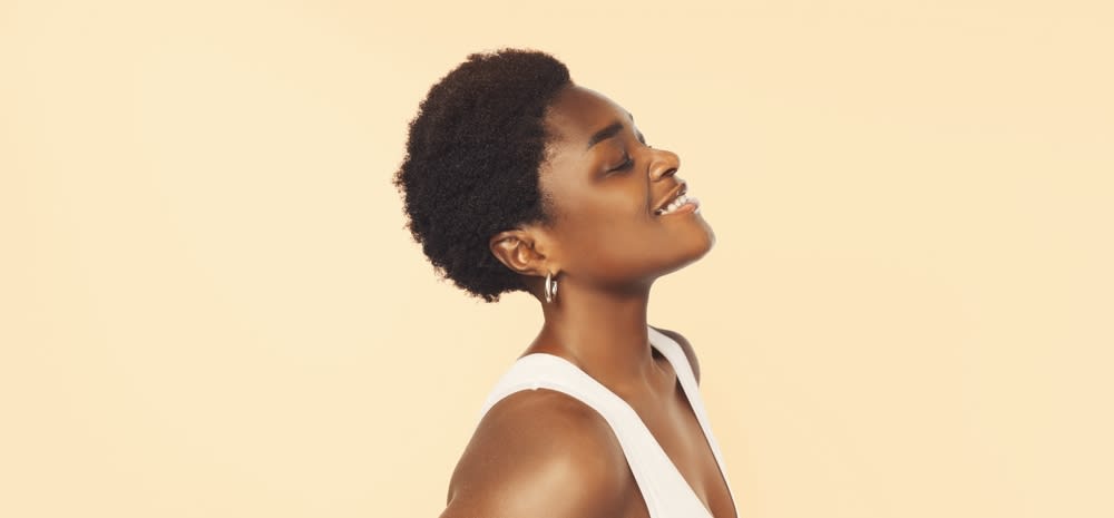 Imagem de mulher com maquiagem neutra e pose de perfil sorrindo