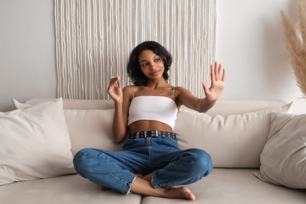 Imagem de mulher sentada em um sofá, ela está pintando as unhas e olhando o resultado