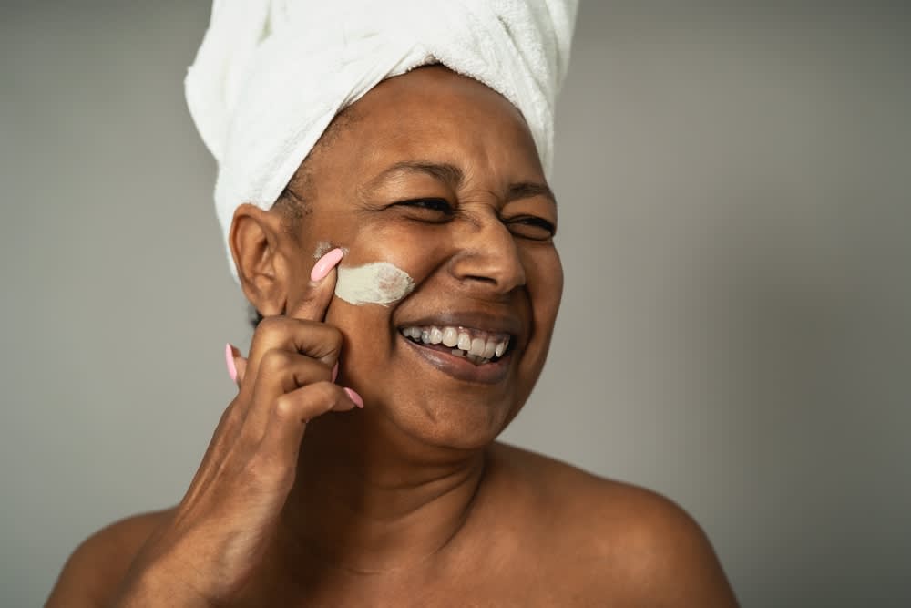 A imagem mostra uma mulher aplicando um produto de skincare na pele