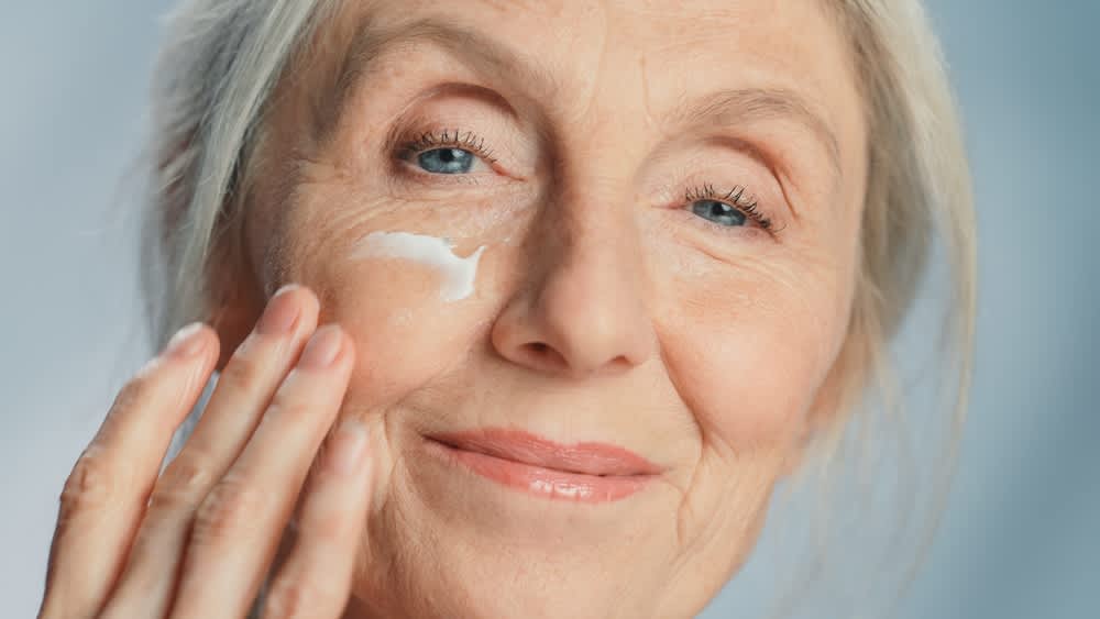 A imagem está com zoom no rosto de uma mulher, ela está aplicando um creme na pele