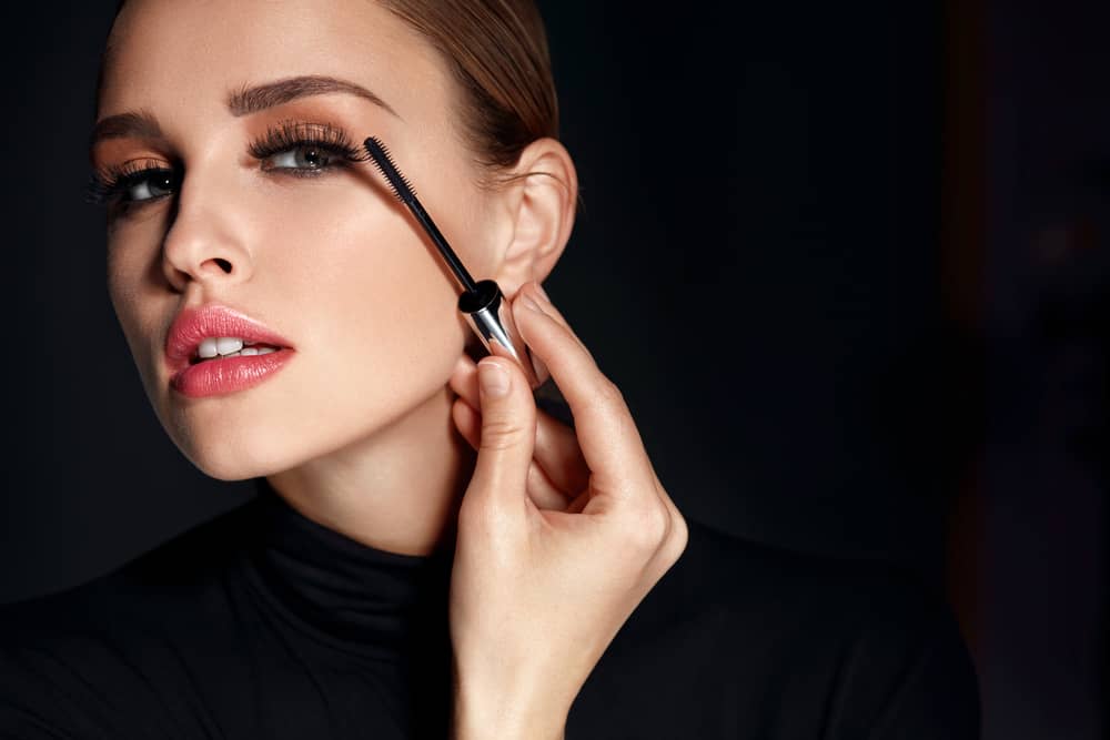 A imagem mostra uma mulher aplicando máscara de cílios