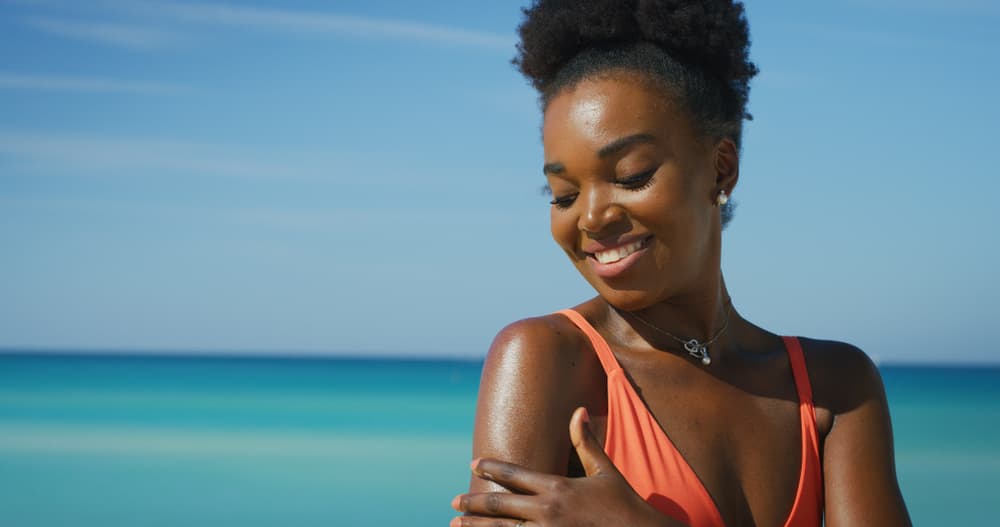 A imagem mostra uma mulher em um dia ensolarado na praia após a rotina de suncare