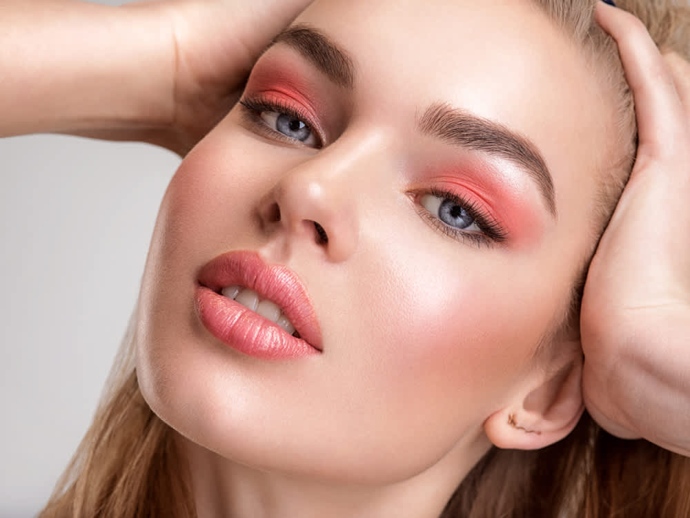 Imagem de mulher com maquiagem em tons de rosa, incluindo os olhos, bochechas e boca