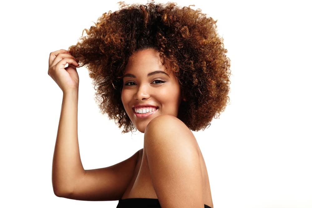 Mulher com cabelo crespo, ela sorri admirando seu cabelo