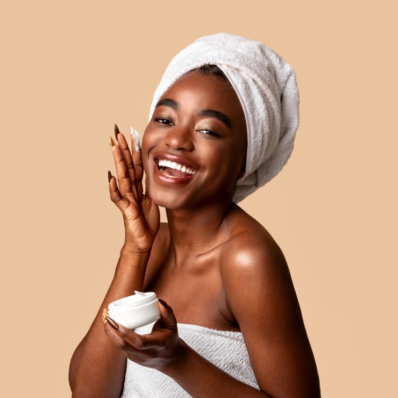 Mulher sorrindo, aplicando creme facial na pele do rosto