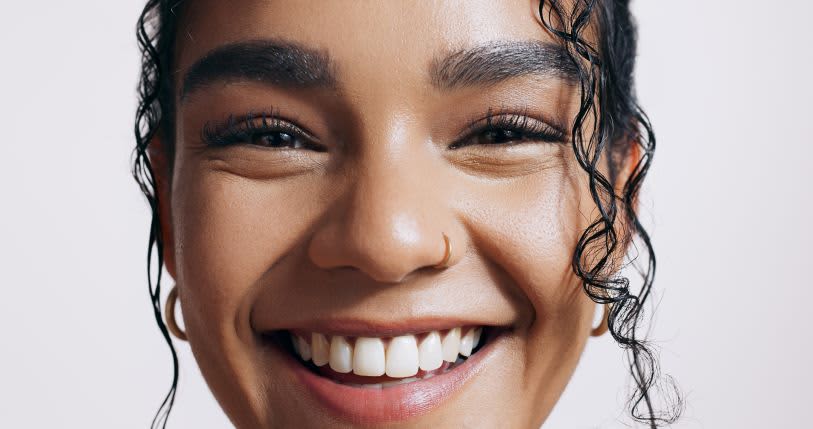 Mulher sorrindo, ela tem cílios naturalmente longos e sobrancelha preenchida