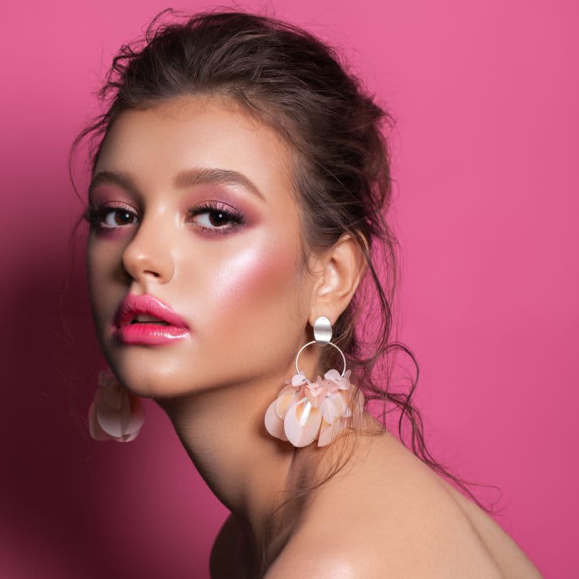 Mulher usando maquiagem com blush, batom e sombra nas cores rosa.