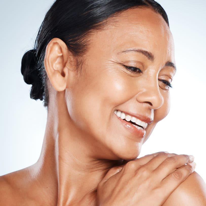 Uma mulher sorridente com pele radiante. Ela parece feliz e confiante. A imagem é bem iluminada e captura a beleza natural da mulher.