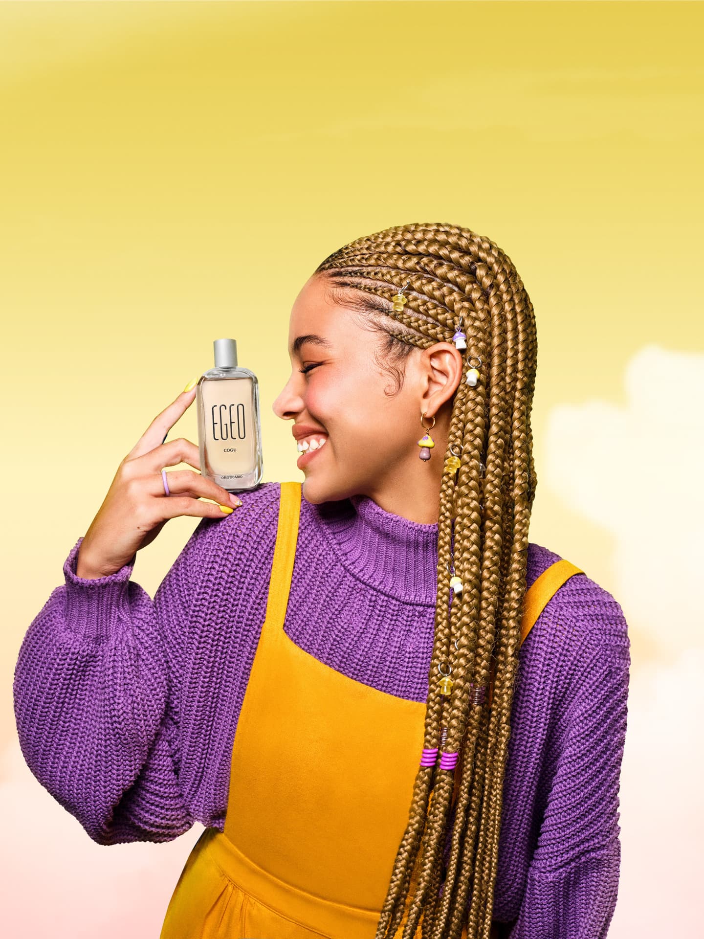 Mulher negra com tranças e roupas nas cores roxo e amarelo segurando um frasco da fragrância Egeo Cogu