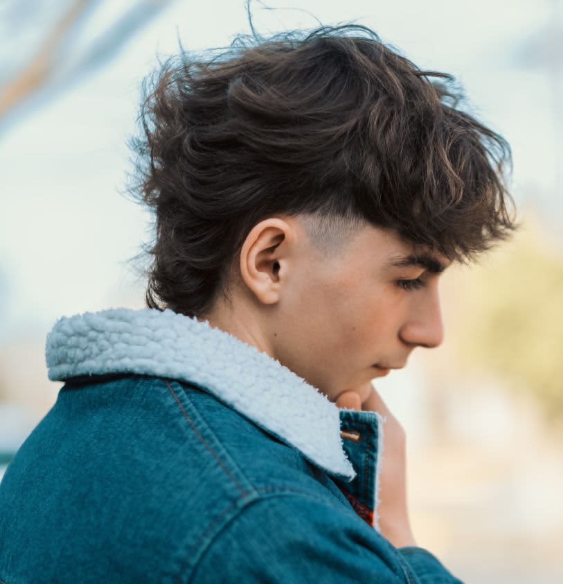 Jovem usando roupas azuis, ele está de costa exibindo um corte mullet curto