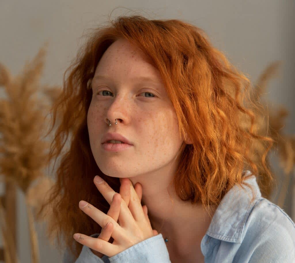 Mulher ruiva com cabelo ondulado e piercing no septo.