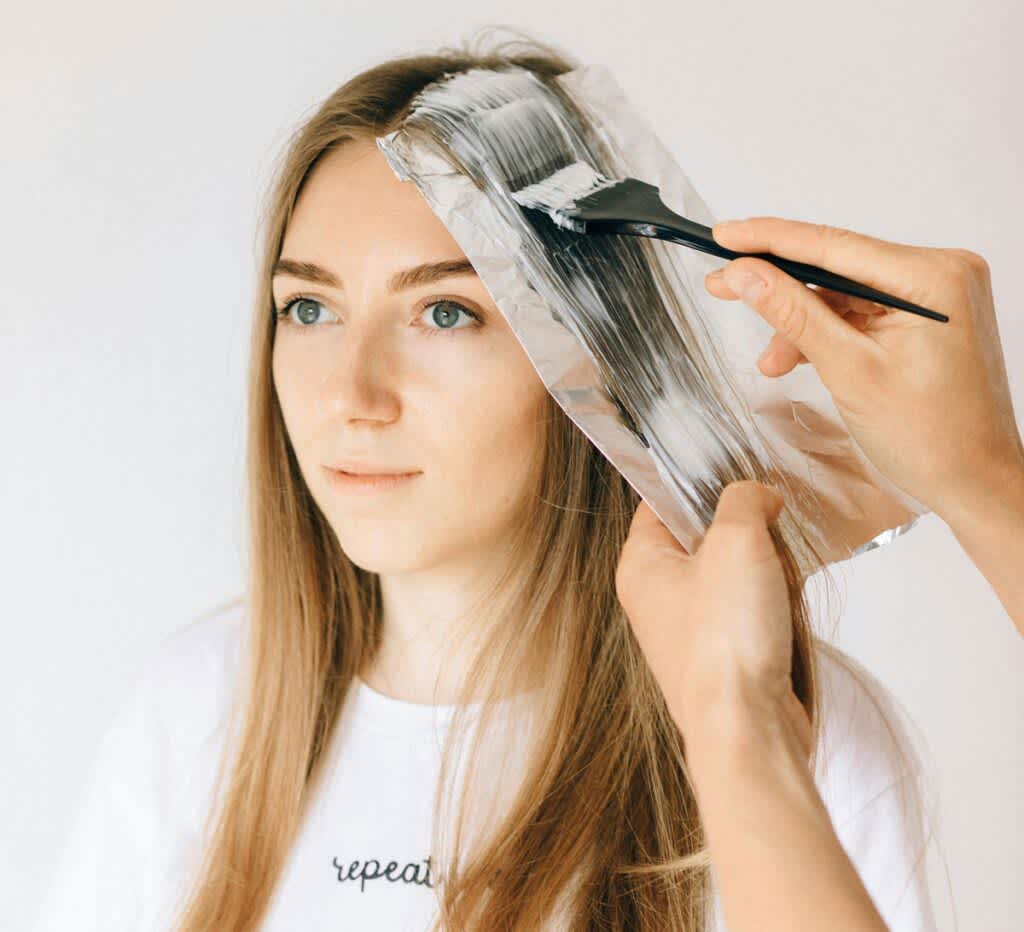 Mulher loira fazendo luzes no cabelo. Alguém está aplicando descolorante em uma mecha do cabelo da mulher. 