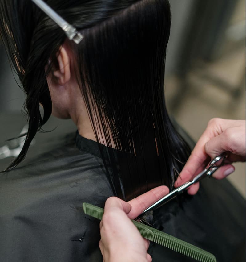 Mulher de costas cortando o cabelo molhado