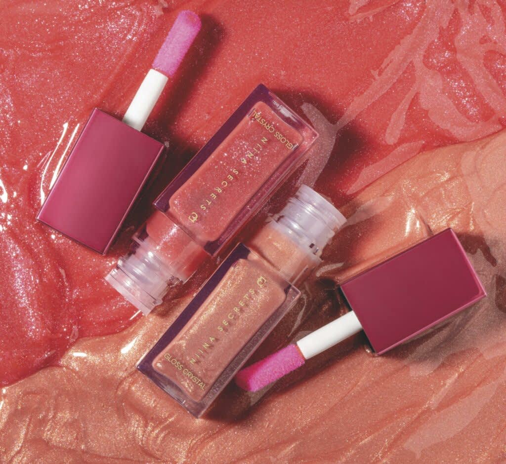 Imagem com fundo pink com textura de gloss e dois glosses da linha Niina Secrets abertos