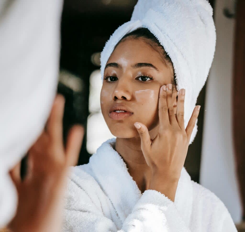 Mulher com toalha na cabeça aplicando creme facial