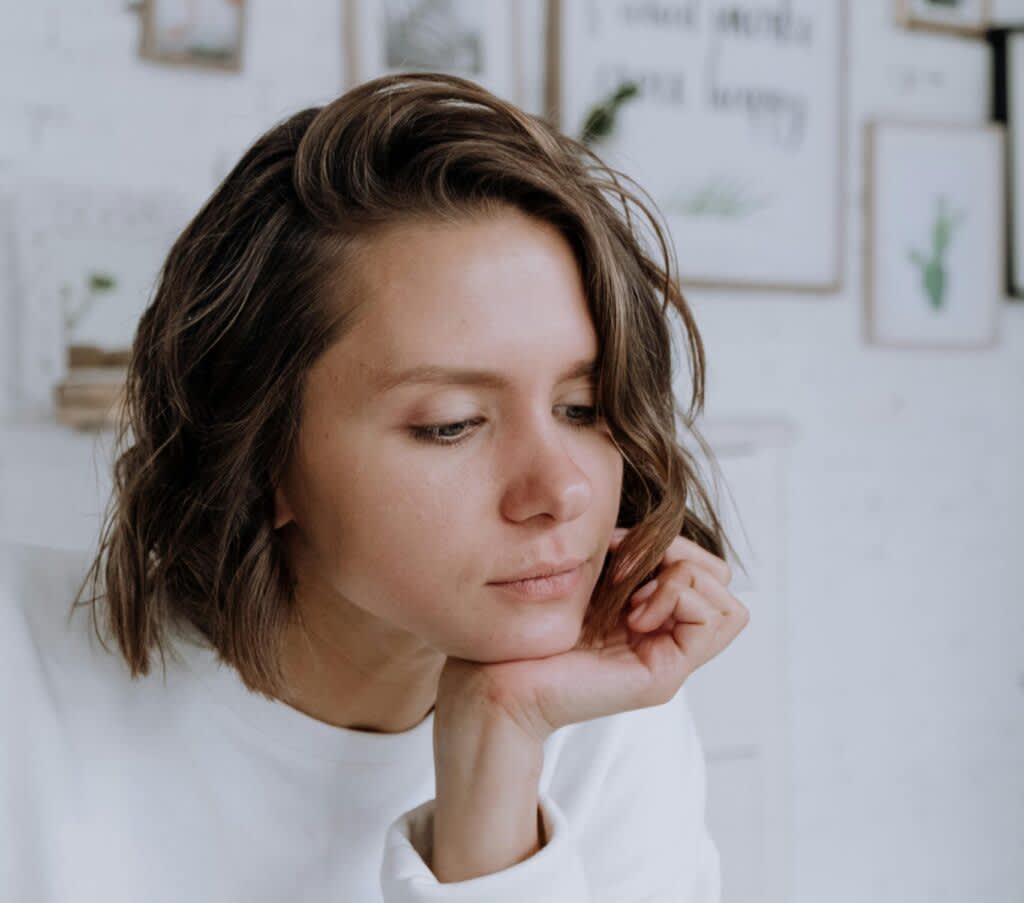 Mulher com cabelo médio e blusa branca com a mão apoiada no rosto