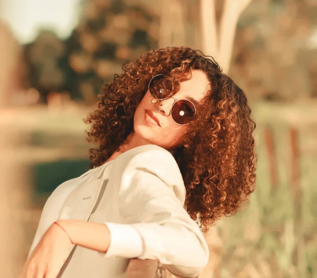 Mulher de cabelos cacehados encostada de costas para uma cerca