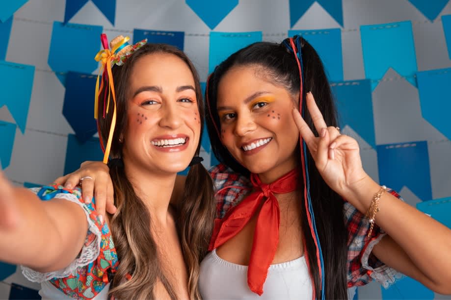 Imagem de duas amigas usando a maquiagem clássica de festa junina com blush marcado e pintinhas feitas com lápis de olho
