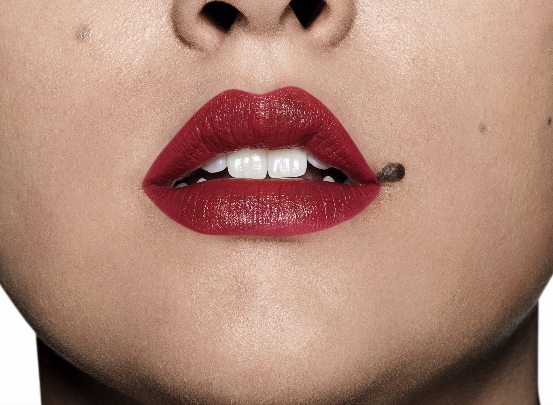 Batom cremoso Intense vermelho. A imagem foca na boca da modelo, que é branca com uma pinta na lateral dos lábios.