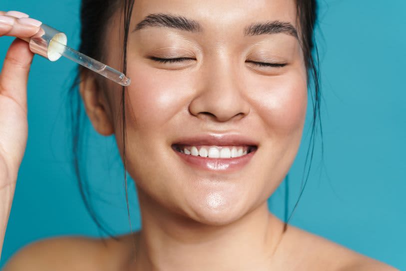 Mulher sorrindo enquanto aplica sérum facial com Retinol na pele