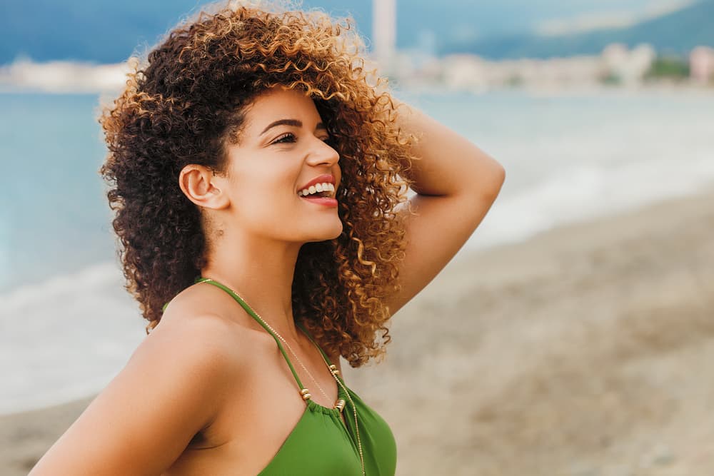 Imagem de mulher com cabelo cacheado e com mechas na praia