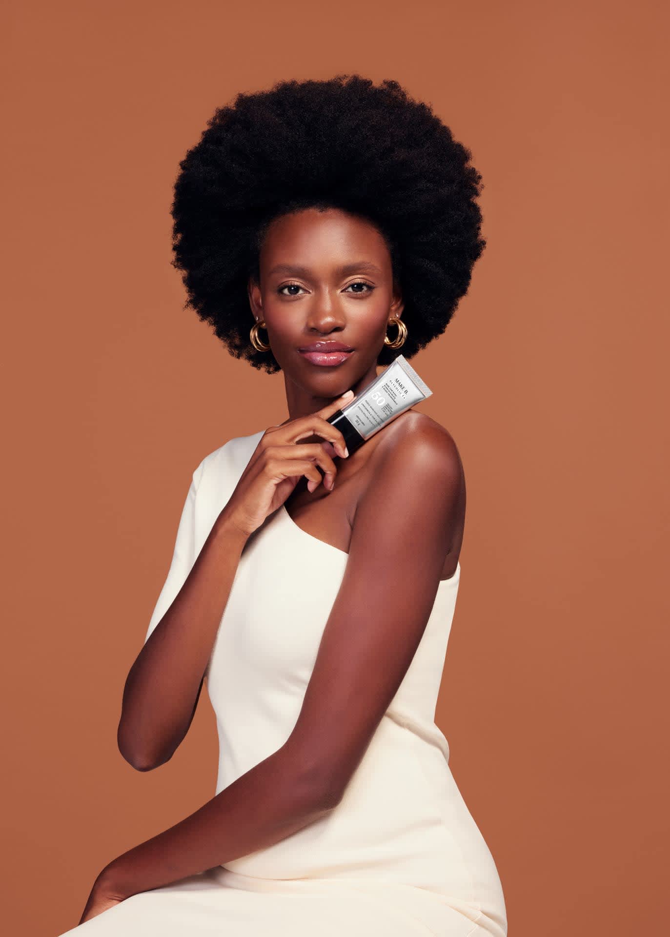 Imagem de mulher segurando a embalagem da base próxima ao rosto para mostrar o resultado de pele uniformizada e com efeito lifting