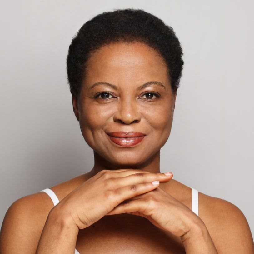Uma mulher negra de meia-idade, com cabelos curtos e sorrindo, posa com as mãos juntas abaixo do queixo.