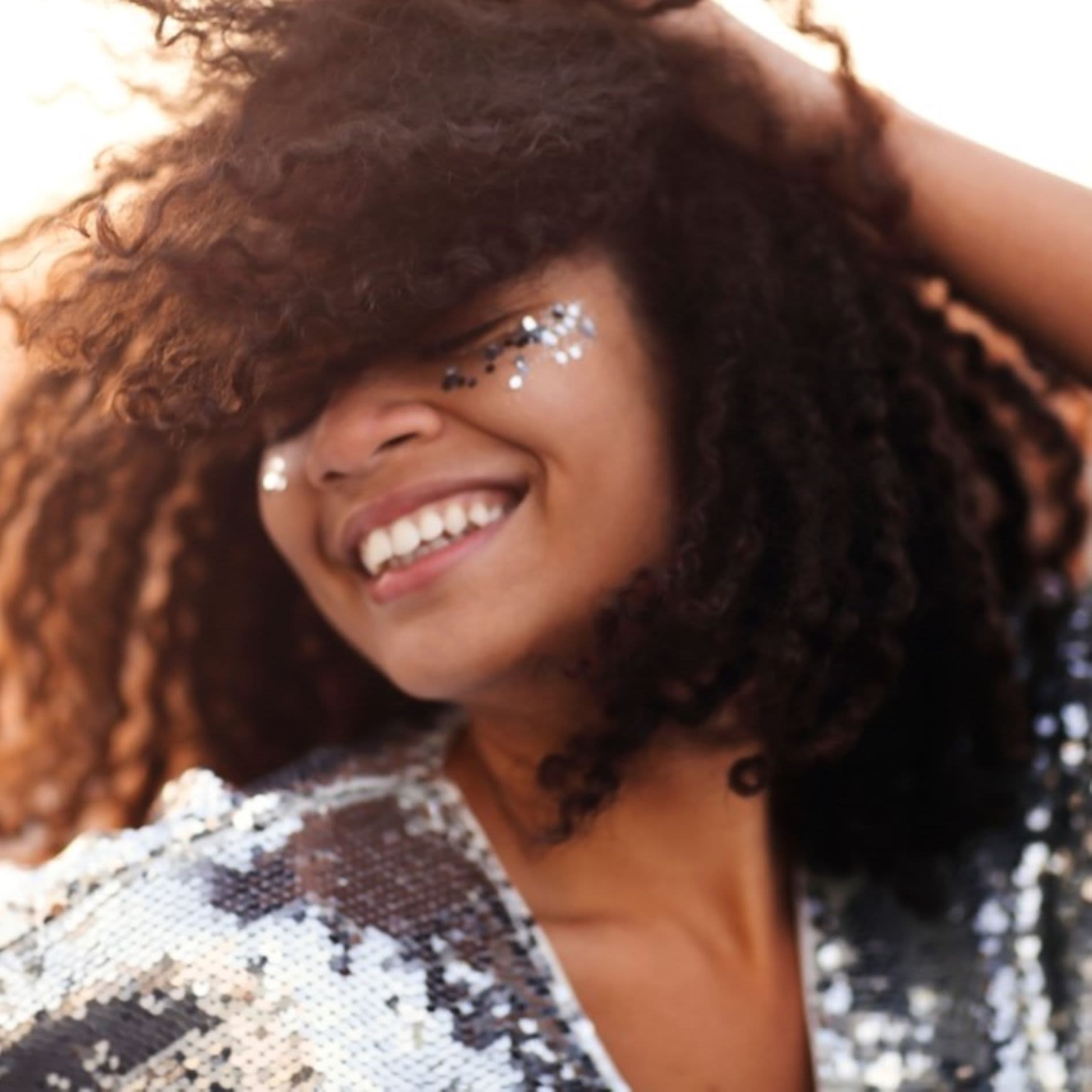 Mulher sorrindo usando roupa de paetê e maquiagem com glitter prateado