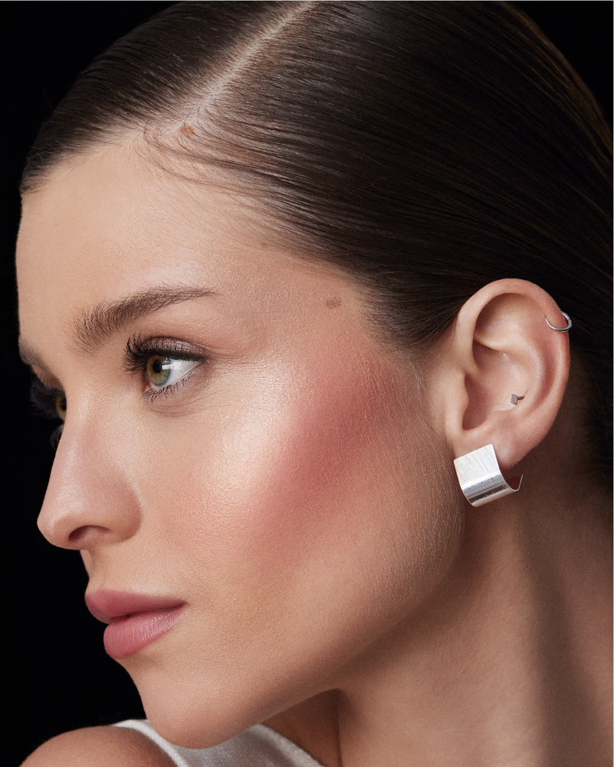Mulher com maquiagem e brincos de prata. Seu cabelo está preso e liso.