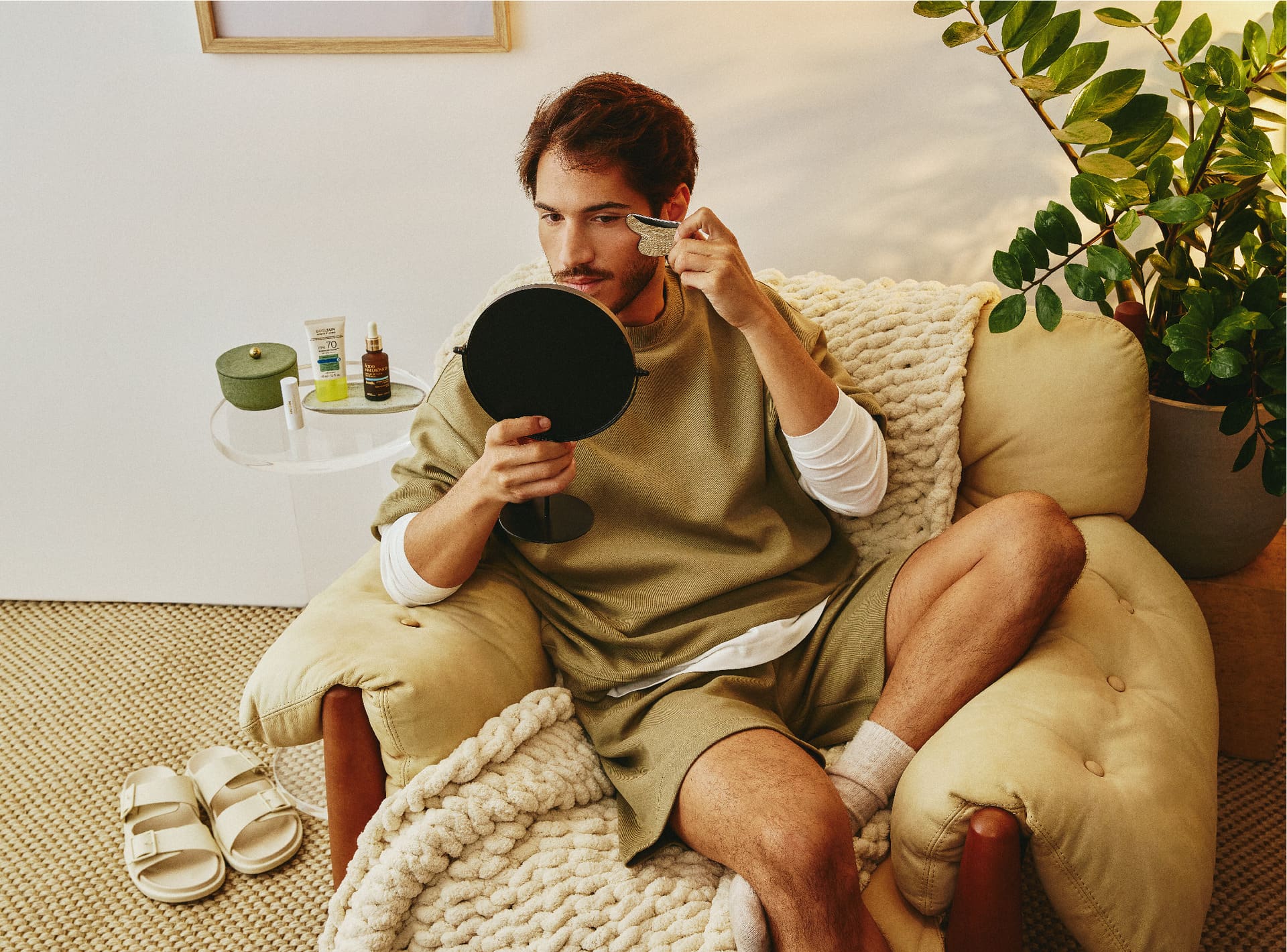 Homem relaxado em sofá enquanto faz uma massagem facial usando o Gua Sha