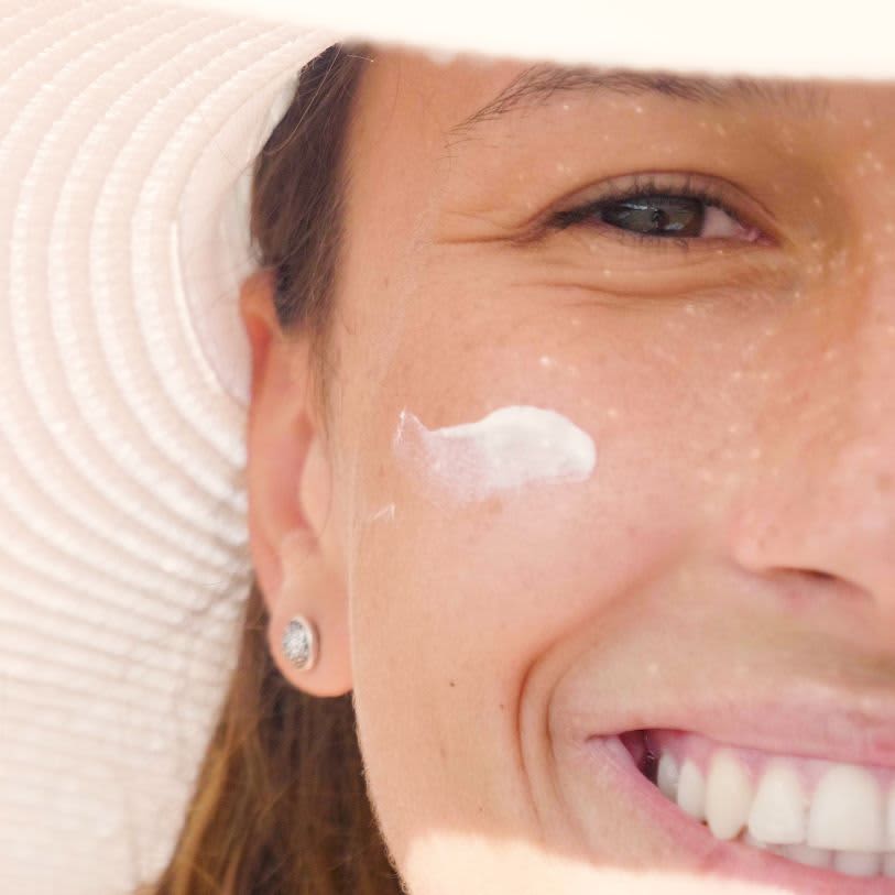 Mulher com chapéu, sorrindo e com protetor solar no rosto
