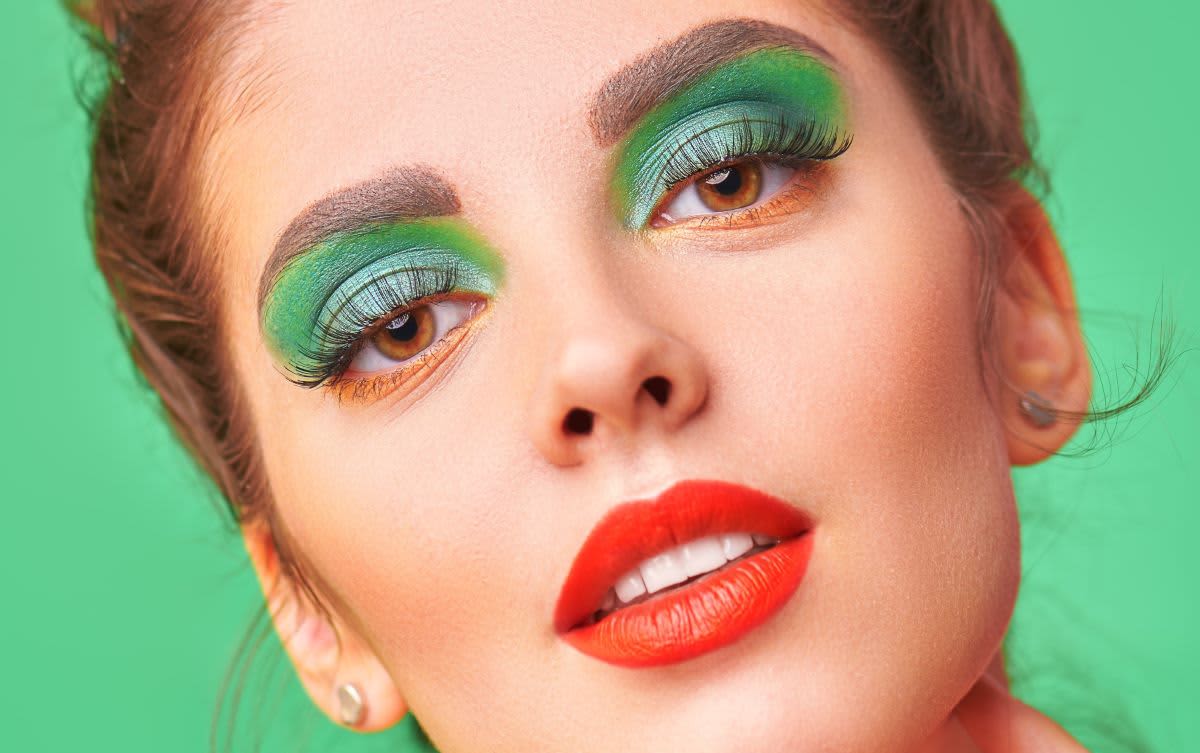Mulher de cabelo castanho, em fundo verde, com uma maquiagem verde e vermelha que ilustra a colorimetria com cores complementares