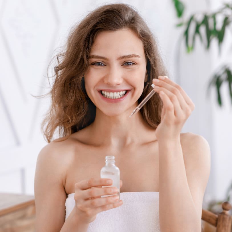 Mulher com cabelo ondulado em banheiro aplicando sérum facial na pele