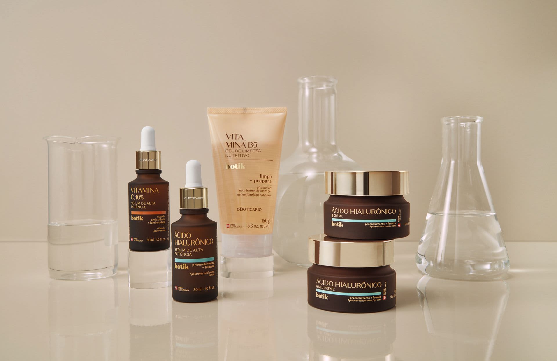 Uma variedade de produtos da linha Botik de O Boticário dispostos sobre uma superfície clara ao lado de vidrarias de laboratório