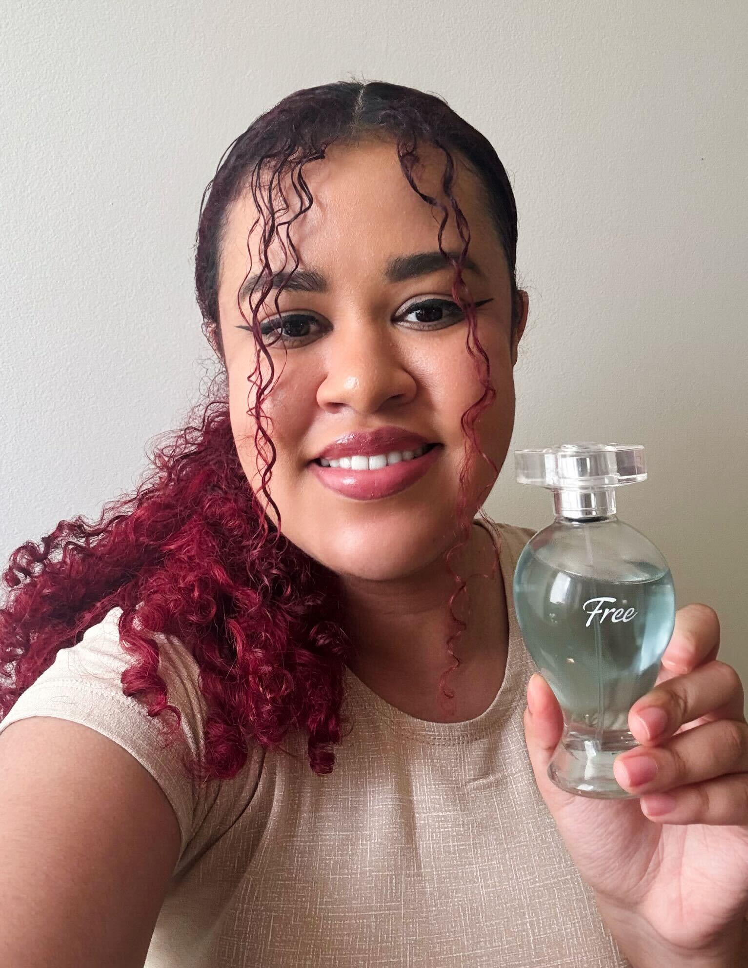 Uma mulher sorridente com cabelo ruivo encaracolado segurando um frasco de“Free”.