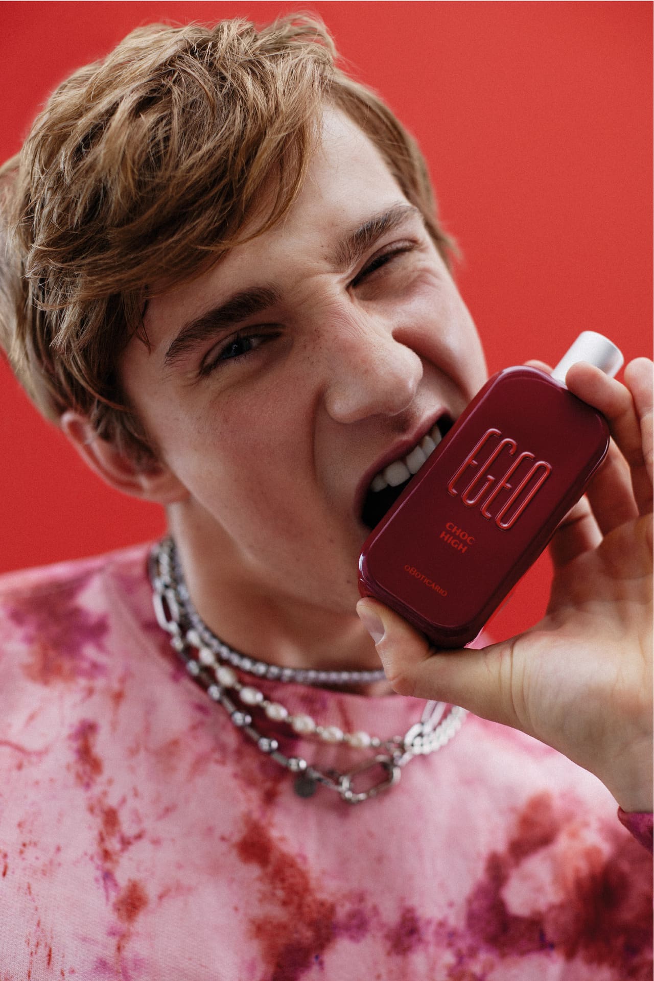 Homem simulando mordida no frasco da fragrância Egeo Choc High que é inspirada nos cheiros de morango e chocolate