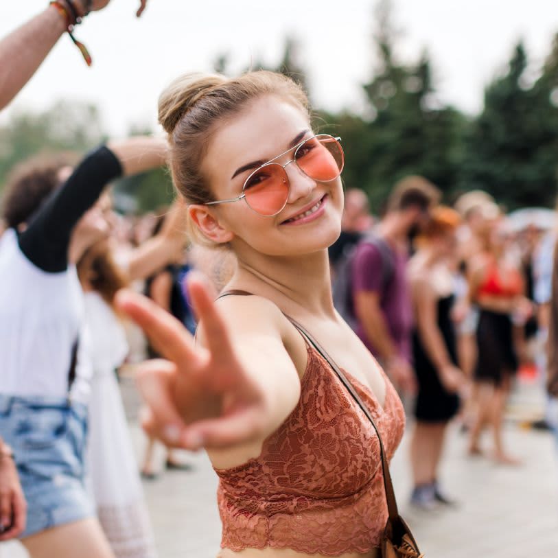 Mulher sorridente de óculos escuros e cabelo preso em um coque alto em um evento ao ar livre.
