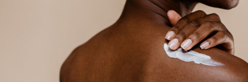 Uma pessoa de costas aplicando creme corporal na pele