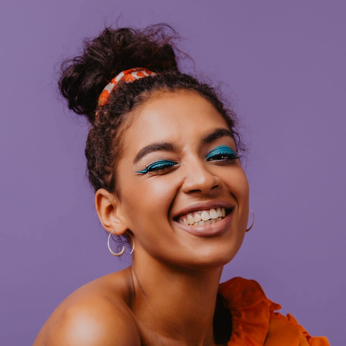 Mulher negra com cabelos amarrados no coque e maquiagem azul nos olhos.