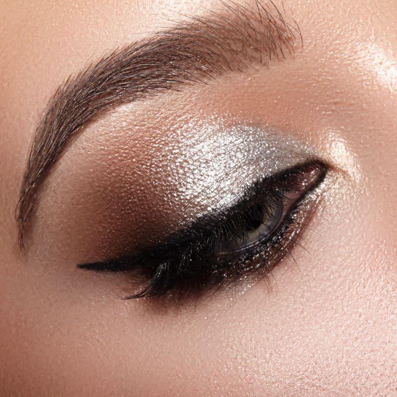 Close de olho com maquiagem metálica prateada e delineado preto, destacando brilho e textura da pele.