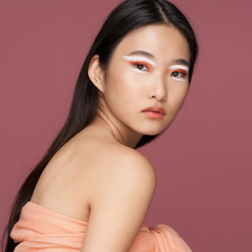 Mulher asiática usando maquiagem com sombra laranja e delineado branco